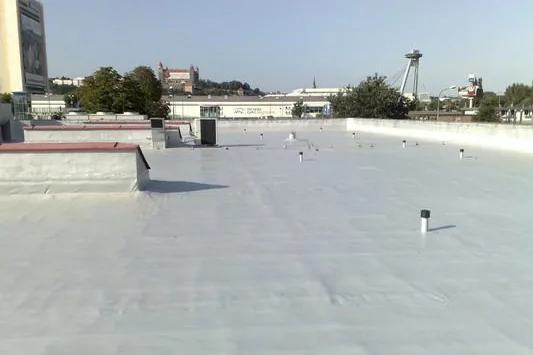 Plochá strecha so svetlou fóliou, v pozadí panoráma mesta